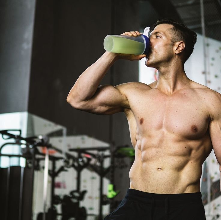 a fit man showing his fit body with abs while drinking his greens 